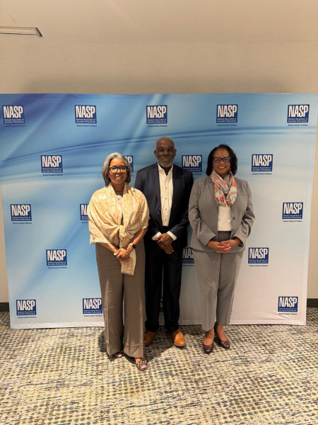Three women in business attire standing together at a UCP branded event backdrop